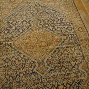 Muted navy blue and tan medallion rug with complex patterns on distressed wood plank flooring.