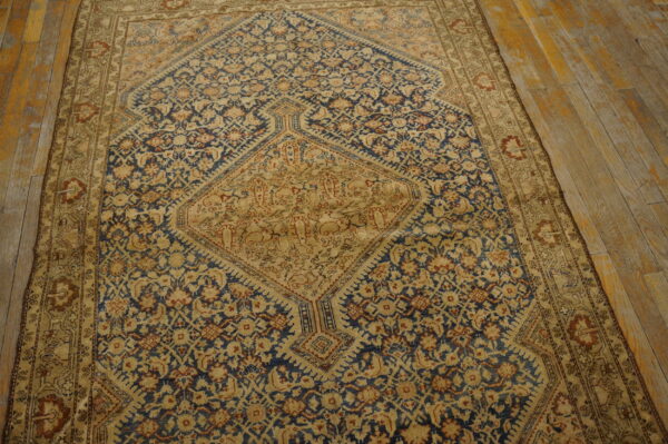 Muted navy blue and tan medallion rug with complex patterns on distressed wood plank flooring.