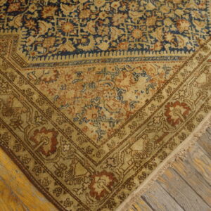 Ornate patterned rug corner in gold, blue, and rust resting on distressed wood planks.