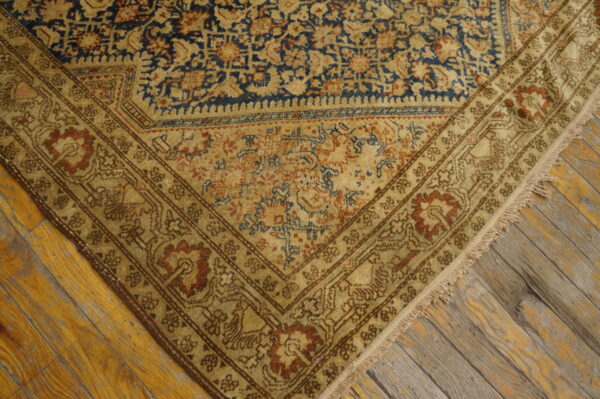 Ornate patterned rug corner in gold, blue, and rust resting on distressed wood planks.