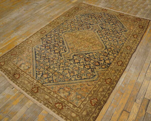 Traditional tan and navy blue rug with dense floral patterns and a central medallion on distressed wood floors.