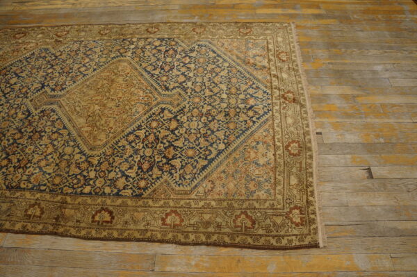Low-pile tan and blue traditional rug with a large medallion on heavily worn wood floors.