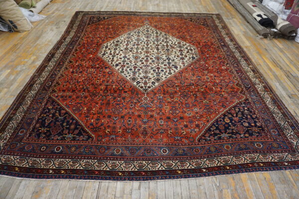 Red patterned rug with a central ivory medallion and navy corners lies on light-colored wood flooring.