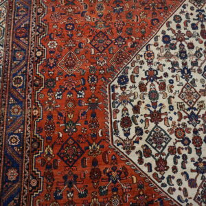 Close-up of a patterned rug featuring a diagonal split between dense ivory and terracotta red fields.