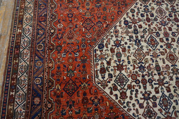 Close-up of a patterned rug featuring a diagonal split between dense ivory and terracotta red fields.