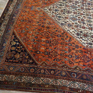 Geometric patterned rug in rust, cream, and navy blue covering light-colored wide plank flooring.