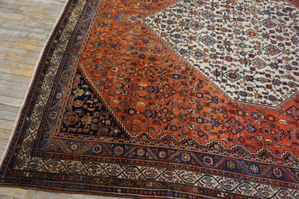 Geometric patterned rug in rust, cream, and navy blue covering light-colored wide plank flooring.
