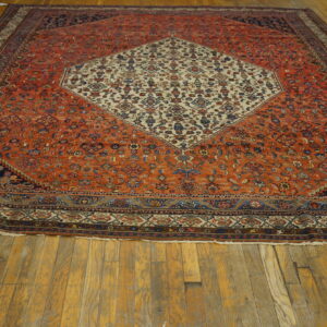 A large low-pile rug with an orange field and cream center medallion lies on wide plank wooden floors.