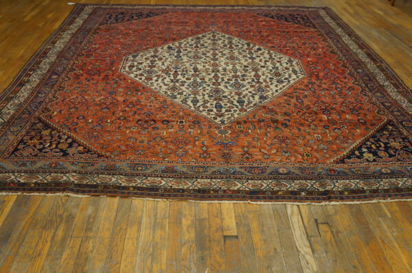 A large low-pile rug with an orange field and cream center medallion lies on wide plank wooden floors.