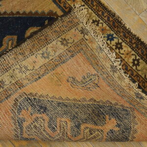 Geometric navy blue and tan rug corner lifted to show the woven peach colored backing on wood flooring.