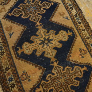 Intricate blue and brown geometric rug with a tan field lies partially on distressed blonde wood flooring.