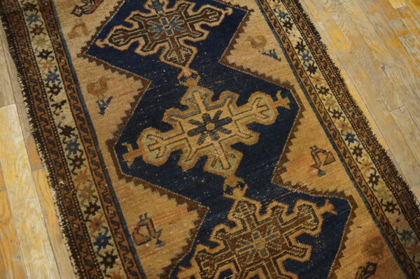 Intricate blue and brown geometric rug with a tan field lies partially on distressed blonde wood flooring.