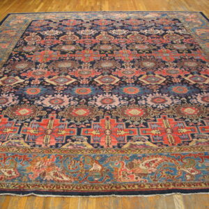 Large area rug with a dark blue field and red, coral, and teal geometric patterns on a wooden floor.
