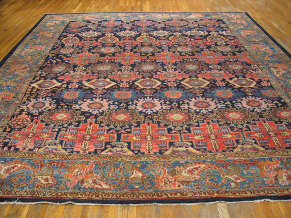 Large area rug with a dark blue field and red, coral, and teal geometric patterns on a wooden floor.