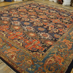 Square rug in navy and rust geometric patterns with a detailed blue border on wide plank wood floors.