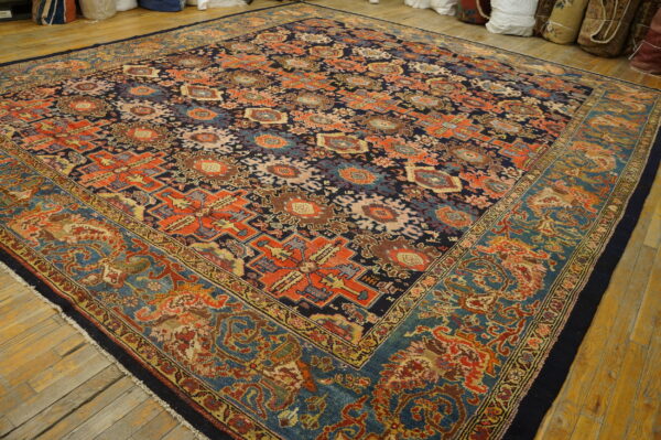 Square rug in navy and rust geometric patterns with a detailed blue border on wide plank wood floors.
