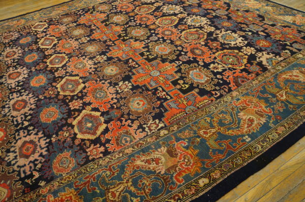 Navy rug with colorful orange, blue, and brown medallions, featuring a wide teal border on wood flooring.