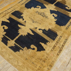 Ornate gold and tan patterned rug with dark blue and brown elements on worn wooden floorboards.