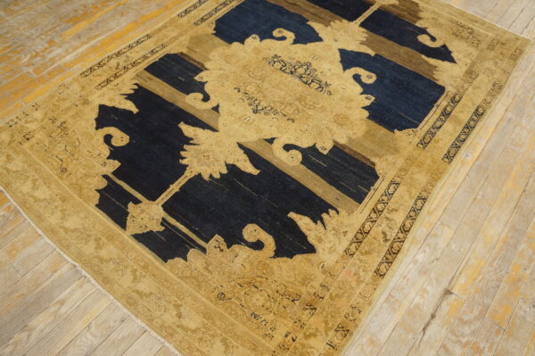Ornate gold and tan patterned rug with dark blue and brown elements on worn wooden floorboards.
