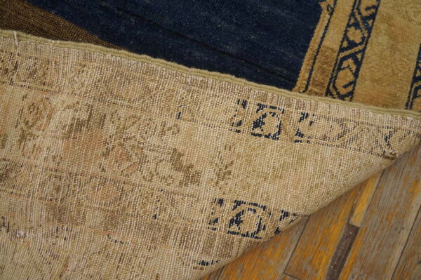 The woven tan backside of a blue and gold low pile rug is visible on wood flooring.