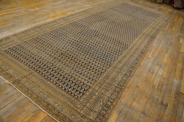Low-pile rug with a repeating dark blue and gold pattern and complex borders on distressed wood flooring.