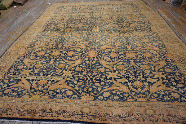 An elaborate dark blue and gold traditional rug featuring stylized floral and animal motifs on wood flooring.