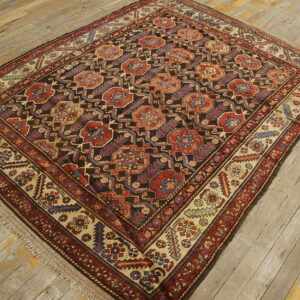 Dark geometric rug featuring red, blue, and tan medallions is placed on rustic wood floors.