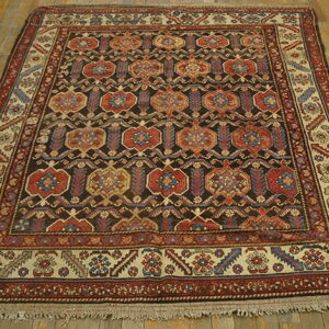 Geometric medallion rug with dark brown, red, and beige colors lying on distressed wood flooring.