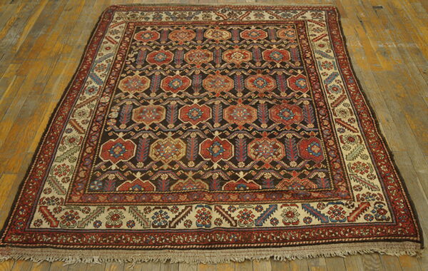 Geometric medallion rug with dark brown, red, and beige colors lying on distressed wood flooring.