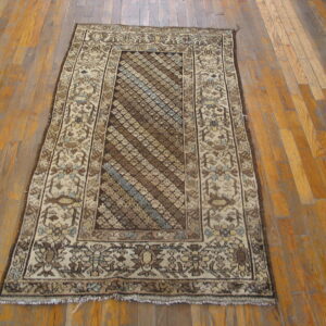 A brown and beige traditional rug featuring diagonal motifs rests on wide plank hardwood flooring.