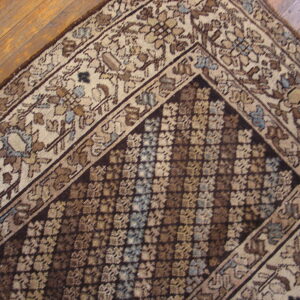 Muted traditional rug with floral borders and a repeating geometric field lies on hardwood.