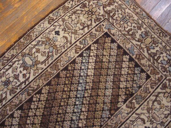 Muted traditional rug with floral borders and a repeating geometric field lies on hardwood.