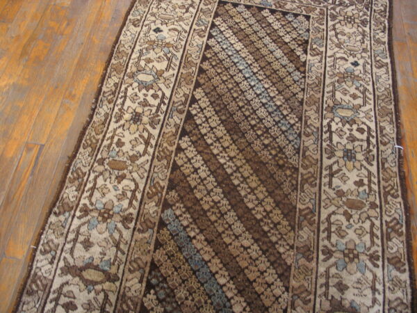 Runner rug featuring muted brown and beige colors, floral borders, and a striped geometric pattern on a wood floor.