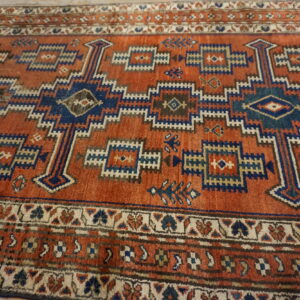 Low-pile orange rug with intricate blue and cream geometric stepped and tribal patterns.