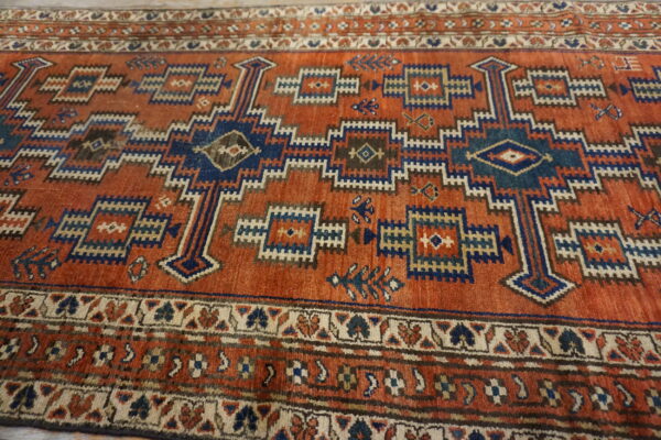 Low-pile orange rug with intricate blue and cream geometric stepped and tribal patterns.