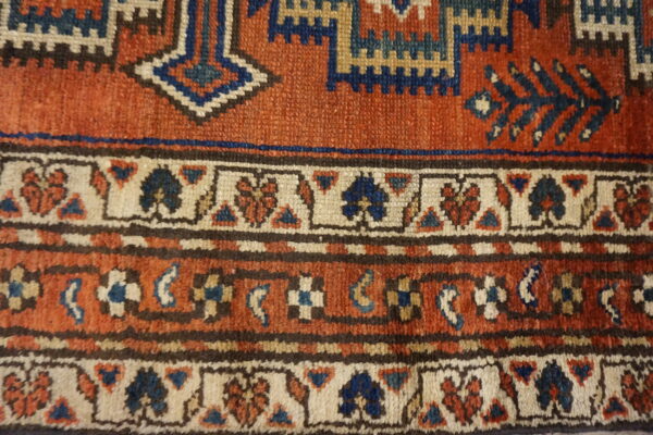 Rust-colored rug detail with navy and cream geometric and stylized floral motifs in multiple borders.