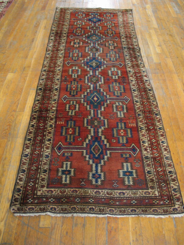 Red runner rug featuring blue and tan geometric patterns on light-colored wood floorboards.