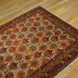 Corner view of a multicolored traditional patterned rug with dark red borders on worn yellow hardwood.