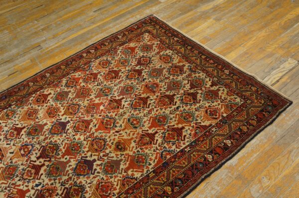 Corner view of a multicolored traditional patterned rug with dark red borders on worn yellow hardwood.