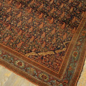 Ornate low-pile rug with a navy field, rust paisley designs, and blue-green borders on light wood flooring.