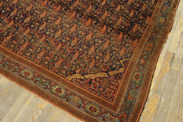 Ornate low-pile rug with a navy field, rust paisley designs, and blue-green borders on light wood flooring.