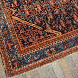Ornate navy rug with rust and teal borders featuring a dense pattern, resting on distressed gray wood.