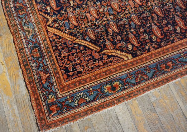 Ornate navy rug with rust and teal borders featuring a dense pattern, resting on distressed gray wood.