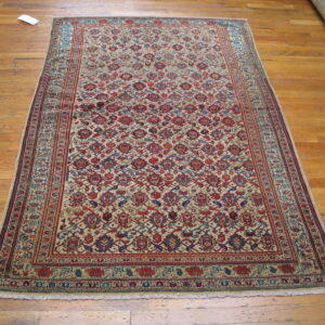 Traditional low-pile rug featuring dense red and blue motifs on a light beige field, lying on wood floors.