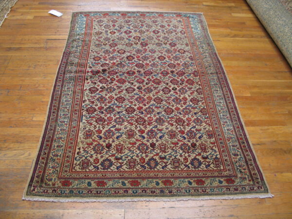 Traditional low-pile rug featuring dense red and blue motifs on a light beige field, lying on wood floors.