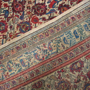 Close-up of a rug featuring muted red and blue floral patterns beside detailed, geometric, multi-color borders.