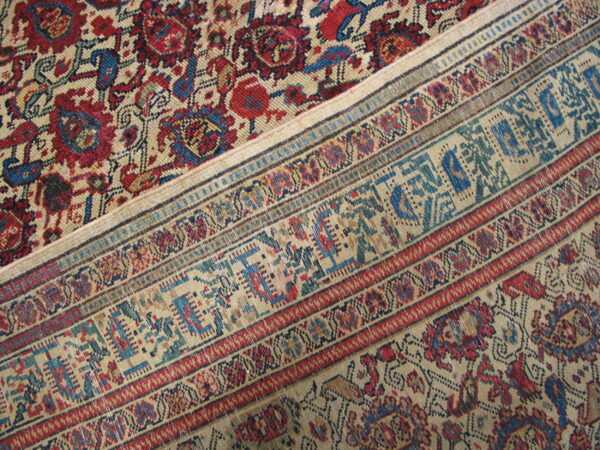 Close-up of a rug featuring muted red and blue floral patterns beside detailed, geometric, multi-color borders.