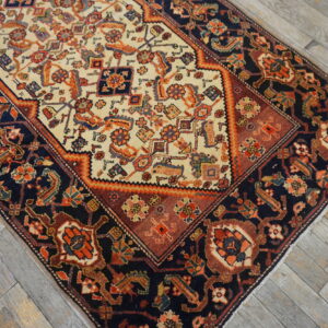 A low-pile area rug with a navy, rust, and ivory medallion pattern sits on weathered wood flooring.