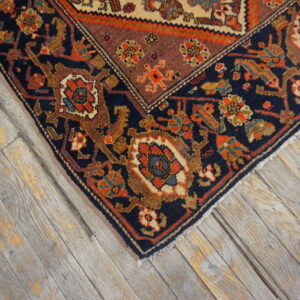 Navy blue and orange patterned rug corner on worn, rustic gray wood plank flooring.