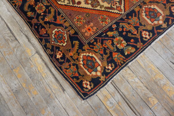 Navy blue and orange patterned rug corner on worn, rustic gray wood plank flooring.
